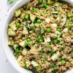 Feral salad in a bowl tossed with a dressing and zucchini and peas with chopped fresh herbs mixed in