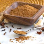 thai 7 spice in a bowl with a small spoon in front of it scattering spice. cloves, garlic by it.