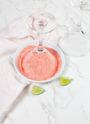 Cocktail glass dipped upside down into a shallow plate with red sugar going on the rim