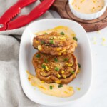 Lobster corn critters on a plate and spicy aioli sauce in a small bowl with lemon zest and chopped green onion.