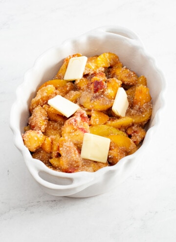 peach cobbler mix in a baking pan with butter pats on top