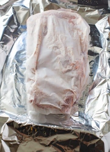 uncooked ribs wrapped in parchment paper, on top of foil