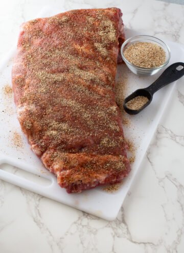 ribs with dry rub on them and a bowl of dry rub and tablespoon of rub