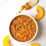 peach bbq sauce in a bowl with bbq brush just dipped in and fresh peaches around