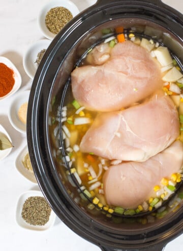raw chicken, broth and veggies in a crock pot bowl