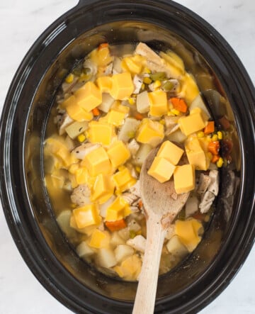 crockpot chicken corn soup cooked with cubed cheese being stirred in