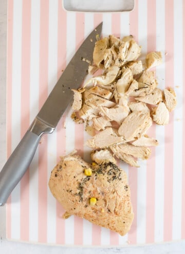 chopped chicken and one whole cooked breast on a cutting board with knife
