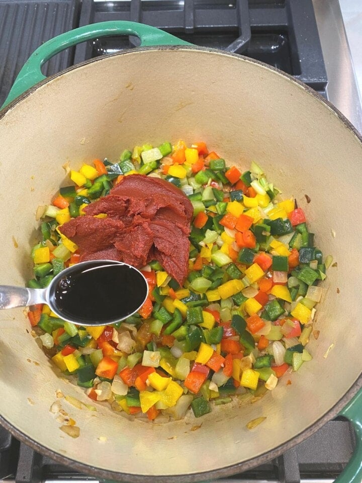 soy sauce and tomato paste being added to vegetables in pan