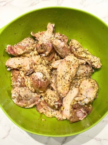 raw wings in a bowl with salt and pepper seasoning mix tossed on them