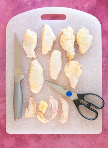 chicken wings cut apart on a cutting board with knife and kitchen scissors