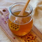 hot honey in a small jar with red pepper flakes around it dripping off spoon