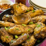 salt and pepper chicken wings with hot honey on them and a dish of hot honey