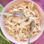 shredded chicken being pulled with two forks in a bowl