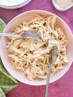 shredded chicken being pulled with two forks in a bowl