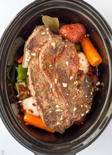seared pot roast and veggies going into crockpot