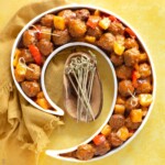 sweet and sour meatballs recipe in a curved dish with toothpicks in some meatballs
