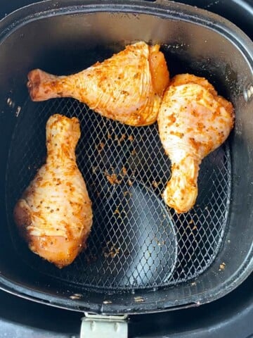 chicken legs coated in seasoning put in air fryer basket