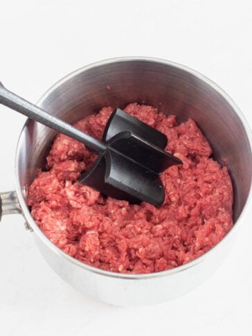 Hamburger Bean cooked in a pan with a meat Chopper being used to break the meat apart