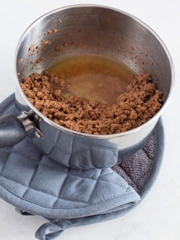 hamburger being cooked in a pan tipped so grease drains