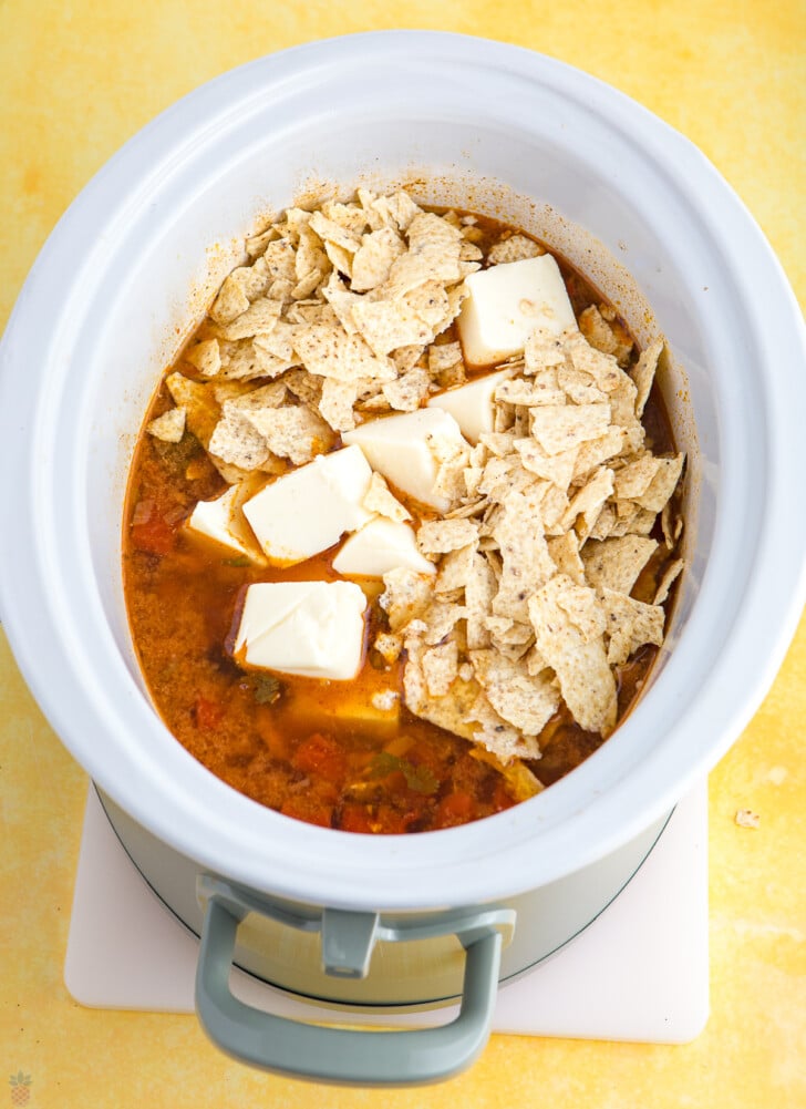 mexican chicken soup in a crock pot cooked with chips and cheese being added.