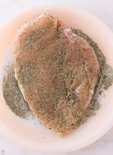 Texas Roadhouse Herb Crusted Chicken raw being dredged in herbs on a pie plate