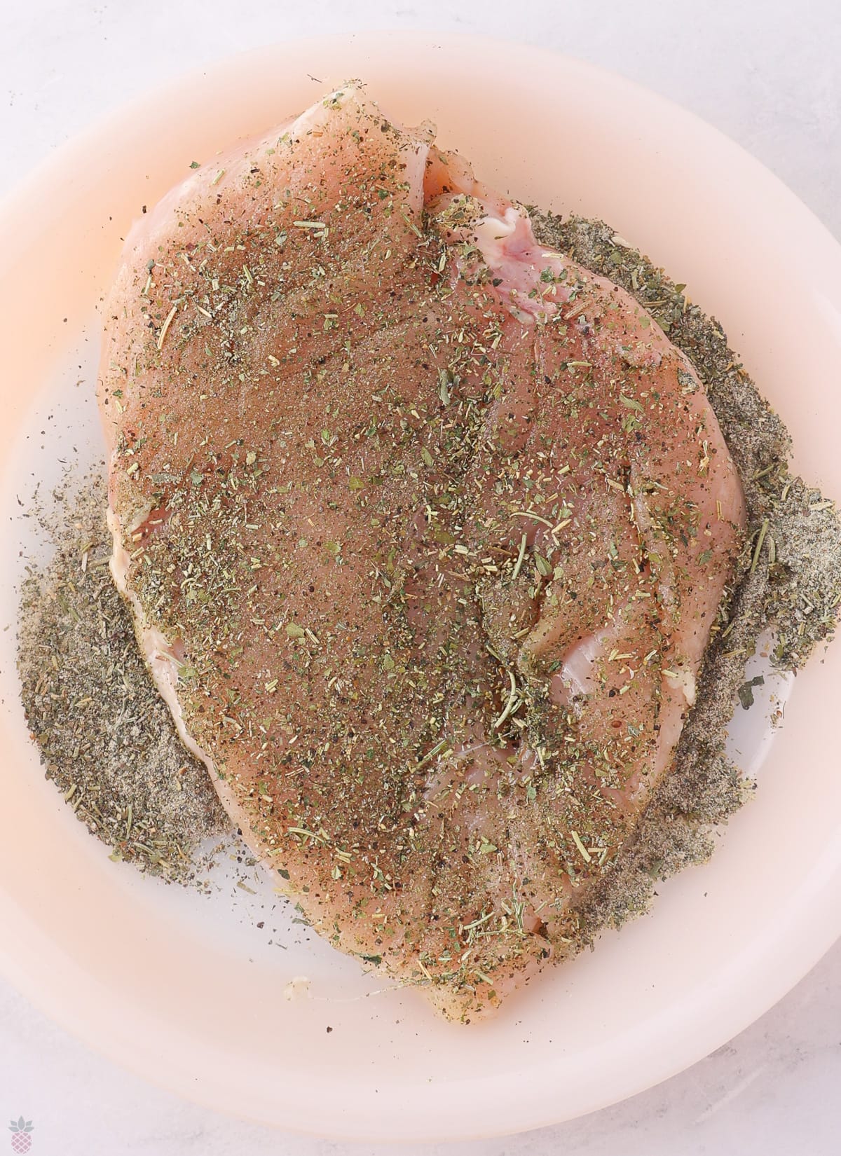 Texas Roadhouse Herb Crusted Chicken raw being dredged in herbs on a pie plate