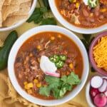 chicken taco soup recipe with cilantro, cheese, radishes and sour cream by it for toppings. a bowl of chips on the side too.