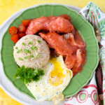 a plate full of chicken tocino with red sauce on top, rice and fried egg on the side