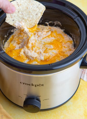 hot crab dip in a crockpot with a chip being dipped in.