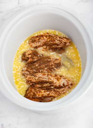 turkey wings with dry rub in a crockpot with gravy ingredients ready to cook.