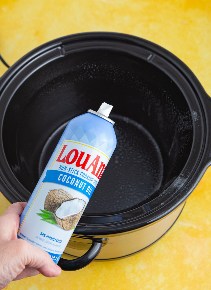 coconut oil spray being sprayed into a slow cooker liner crock