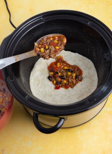 slow cooker mexican casserole ground beef being spooned into a slow cooker
