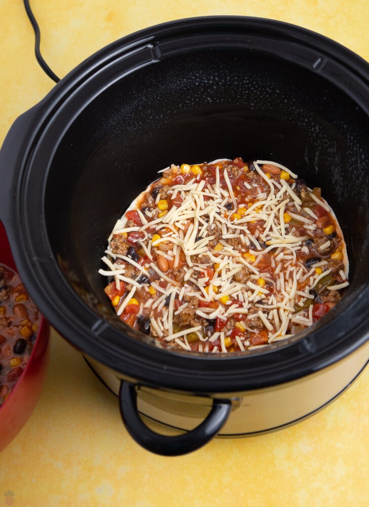 slow cooker mexican casserole ground beef being layered into a round slow cooker