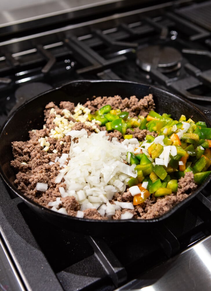 cooked ground beef with garlic, onions and peppers on top in a skillet on the stove top