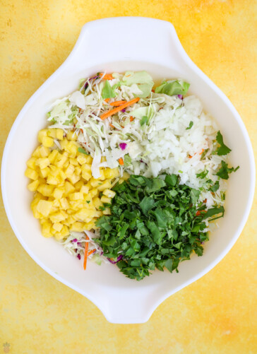 Mexican slaw ingredients in a bowl bag of slaw mix chopped onions cilantro and pineapple