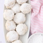 Classic Butterball Cookie rolled in powdered sugar with a bowl of the sugar by the plate