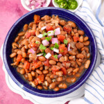 vegetarian crock pot pinto beans in a bowl topped with fresh cilantro, red onions and jalapenos on the side.