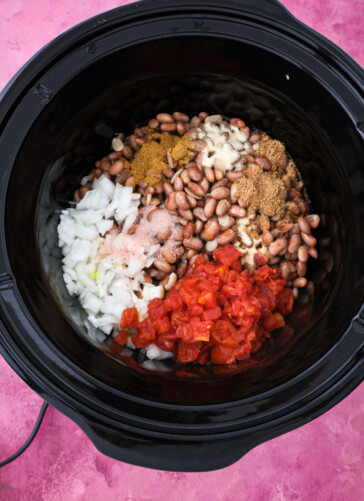 adding beans, seasonings, onions, and tomatoes and chilis to a crock pot.