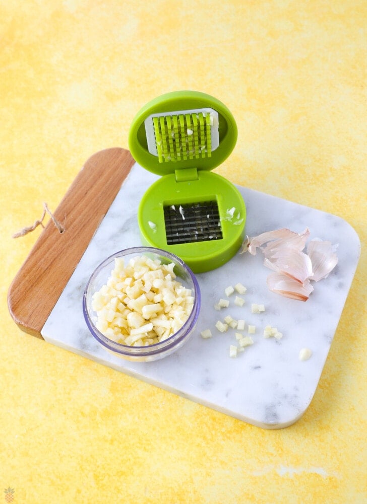 Small mincer used to cut garlic a bowl full of garlic on a cutting board