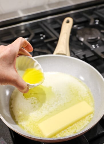 Garlic and a pan melting on the stove with a tablespoon of olive oil being poured in