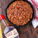 bourbon baked beans with Makers mark bottle next to the skillet full of beans