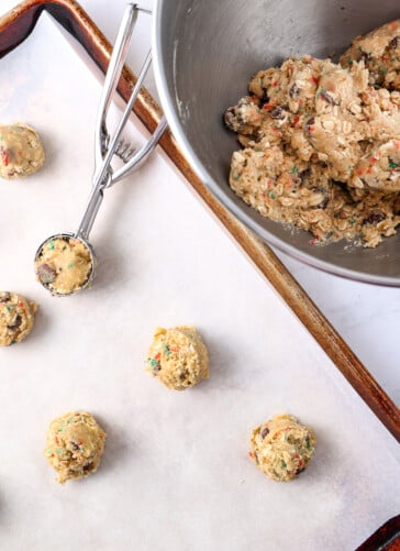 Cookies in a jar mixed together as dough in a bowl a pan of cookies that have been scooped with a cookie scooper on parchment paper ready to bake