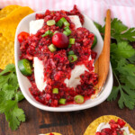 Cranberry salsa poured over cream cheese on a plate with chopped green onions jalapenos and cilantro on the side chips near the plate with cranberry salsa on top of them