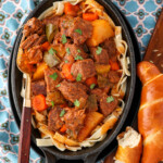 Simple German goulash served over large noodles and a big chunk of pretzel bread next to it