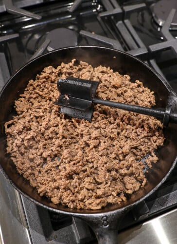 cooking ground beef in a black skillet on the stove.