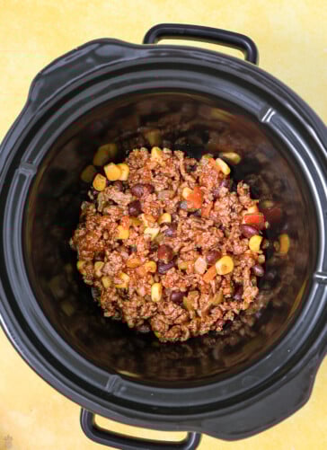 Hamburger beans tomatoes corn chilies all mixed together being put into the bottom of a crock pot