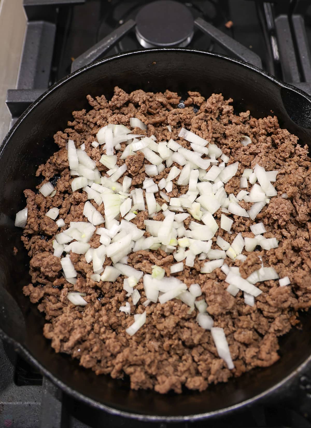Cooked hamburger in a black Skillet on the stove with fresh onions being stirred in