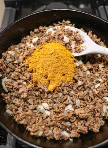 Ground beef that has been cooked in a black Skillet on the stove having taco seasoning stirred in