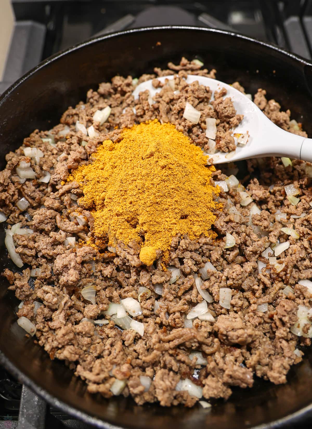 Ground beef that has been cooked in a black Skillet on the stove having taco seasoning stirred in