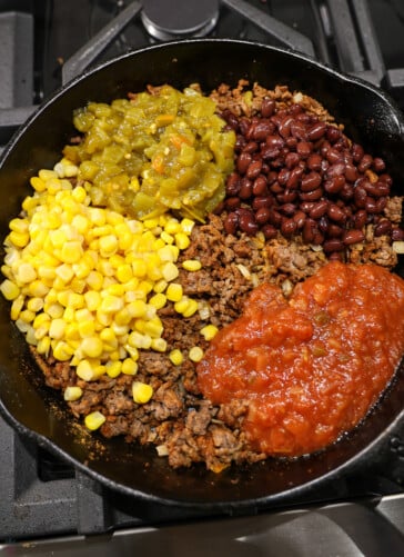 Cooked hamburger in a skillet with beans tomatoes corn and green chilies on top of it
